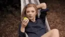 lady swinging in a hammock, eating an apple, with a sly look